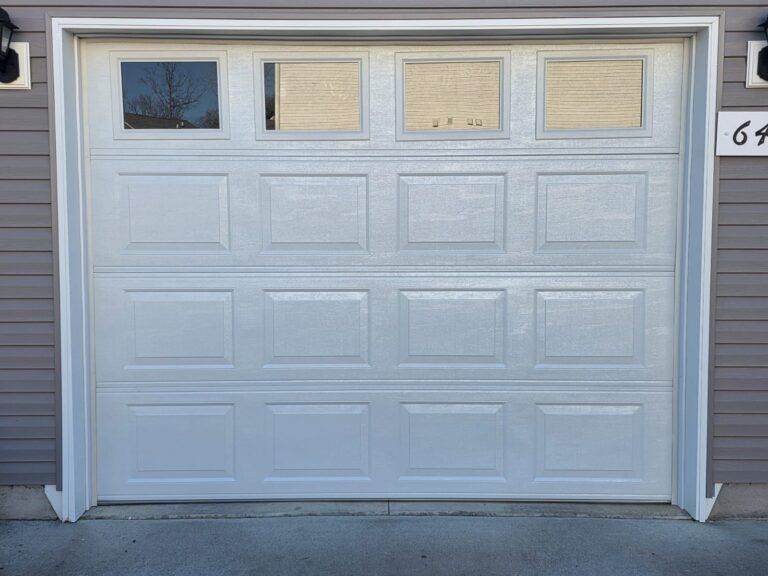 White garage door with a row of windows on a grey-sided home