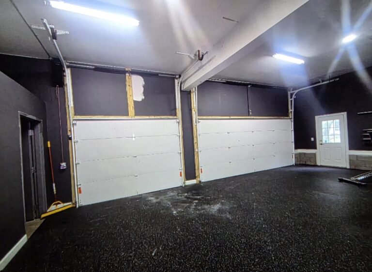 Two white garage doors inside a dark-walled garage gym