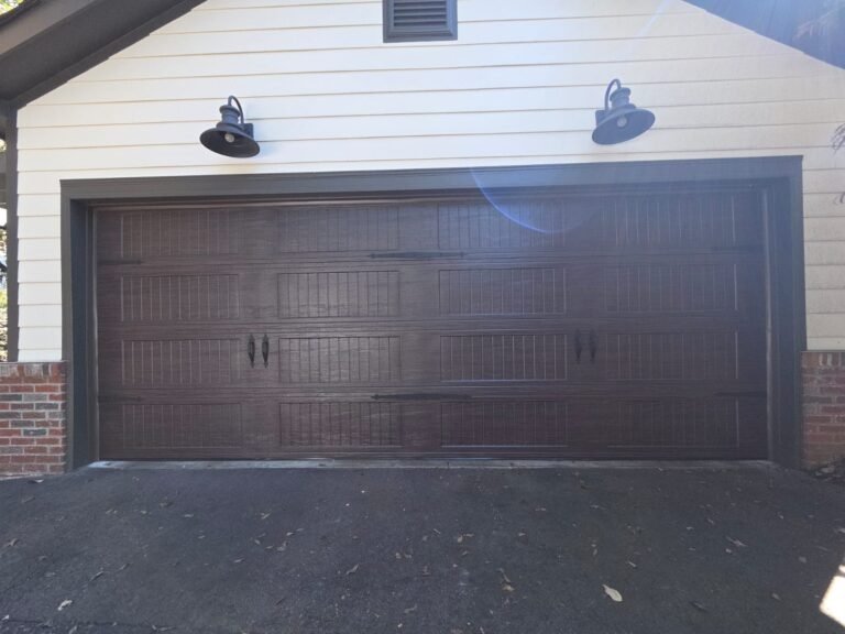 Dark walnut carriage-style garage door with coach lanterns on a tan brick home