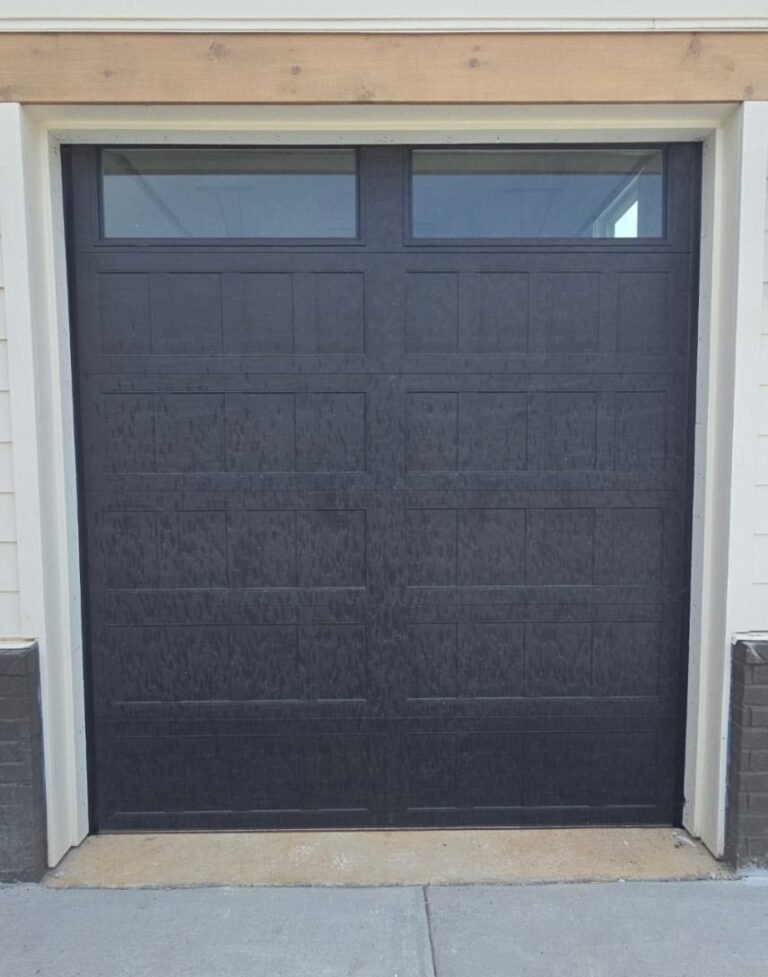 Black raised-panel garage door with windows on a white-sided home