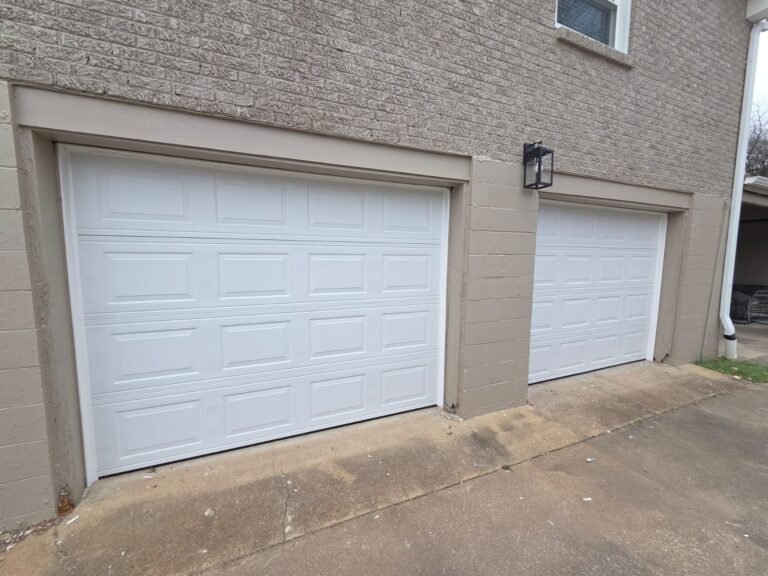 Two white raised-panel garage doors on a beige brick home