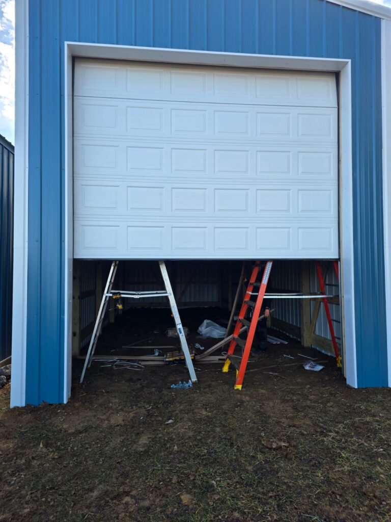 Large white garage door being fitted on a blue metal pole barn